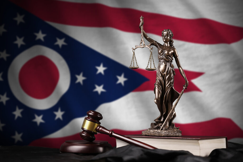 Ohio US state flag with statue of lady justice, constitution and judge hammer on black drapery. Concept of judgement and punishment