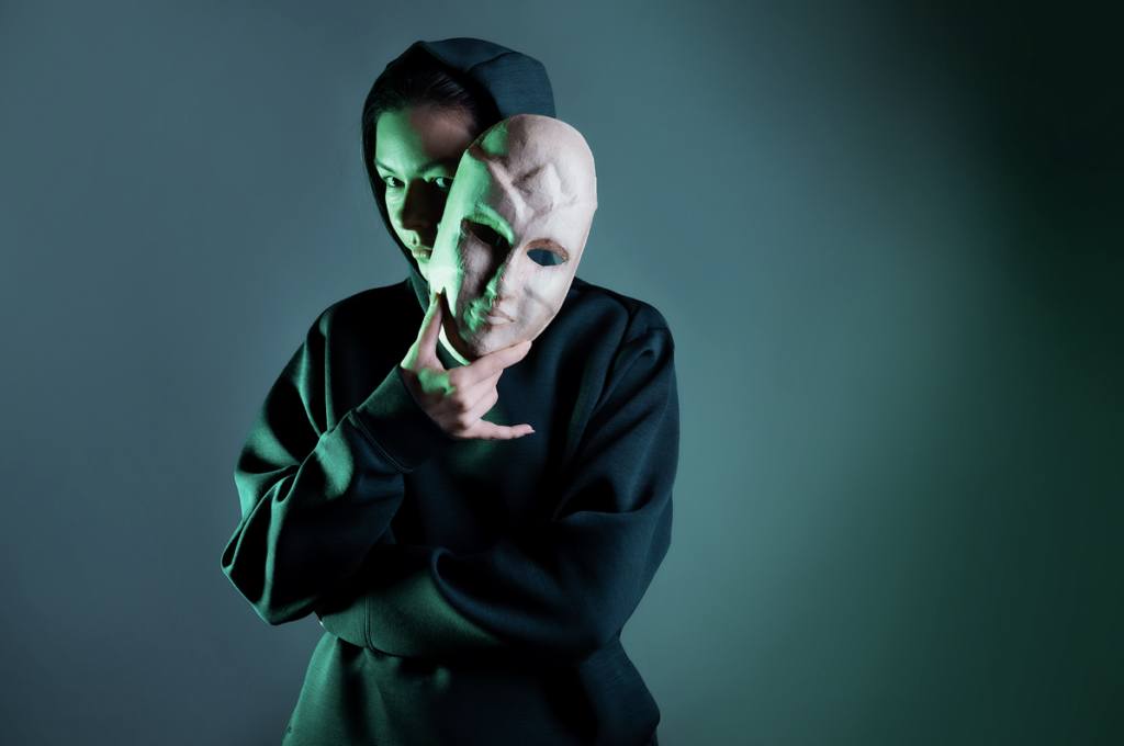 girl in hoodie holding a face mask as an imposter with a green background
